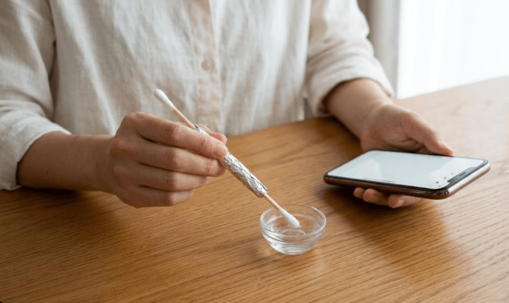 綿棒とアルミホイルで自作したタッチペンの先端を水に湿らせる様子。導電性を高めてスマホの感度を向上させる裏技。