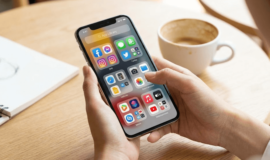 カフェのテーブルで、日本人女性がiPhoneのAppライブラリ機能を使い、自動分類されたアプリを確認している様子。OS固有の便利な整理機能を具体的に示し、
