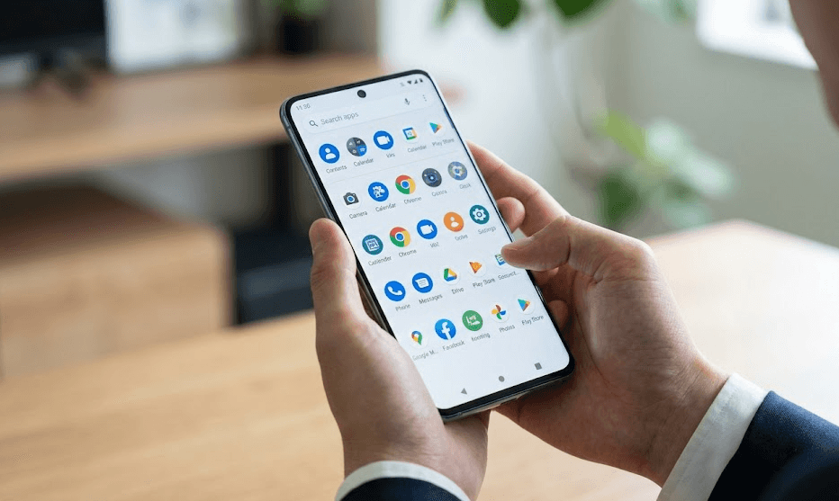 オフィス環境で、日本人男性がAndroidスマートフォンのアプリドロワー（アプリ一覧画面）をスクロールしてアプリを探している様子。Android特有の整理機能を視覚化し、記事の信頼性を高めます。