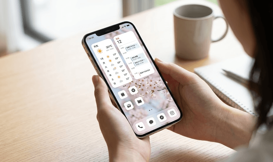明るい室内で、日本人女性がスマートフォンのホーム画面を確認している。画面には、天気予報やカレンダーの予定がひと目で分かるおしゃれなウィジェットが効果的に配置されている。